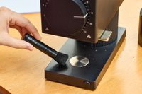 A person brushes coffee grounds from the Fellow Ode Gen 2 Coffee Grinder