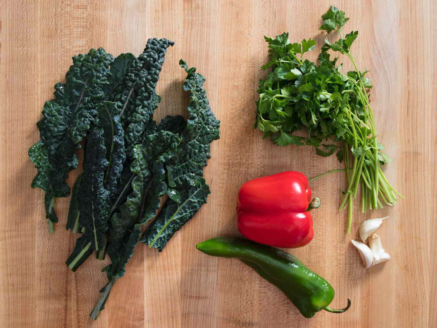 Overhead shot of vegetables for migas: kale, parsley, red bell pepper, garlic, and Anaheim pepper. 