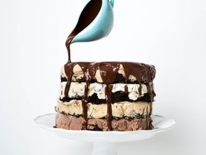 A four-layer ice cream candy bar cake with chocolate sauce being poured over the top. 
