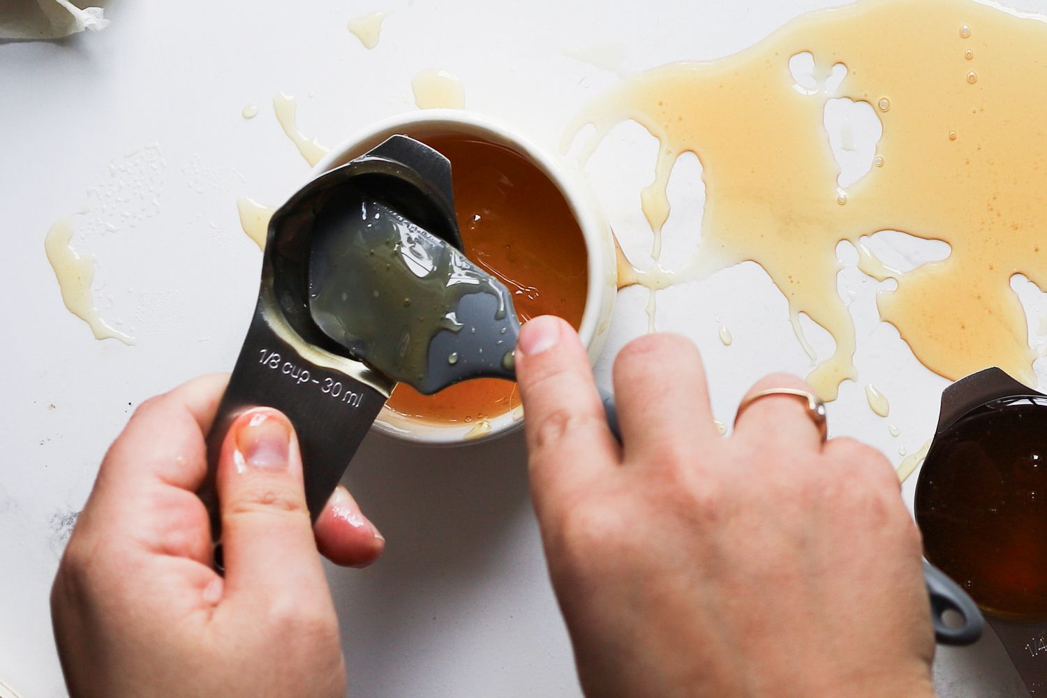 A person pouring honey out of a small measuring cup.