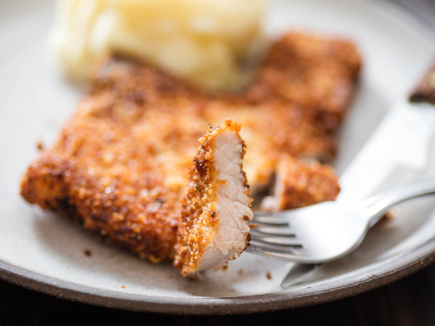 Taking a bite of finished breaded fried pork chops with a fork.