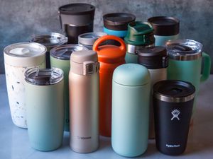 An assortment of fifteen travel mugs sitting on a surface.