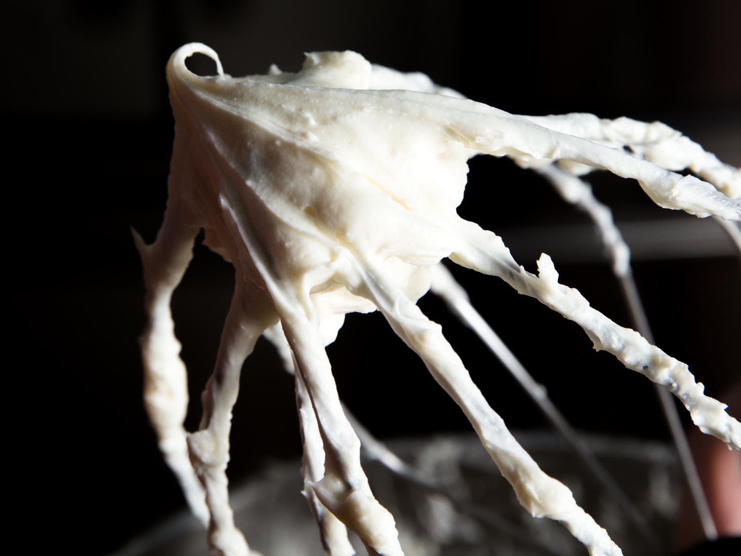 Whipped cream cheese frosting on a whisk attachment looking thick and creamy.