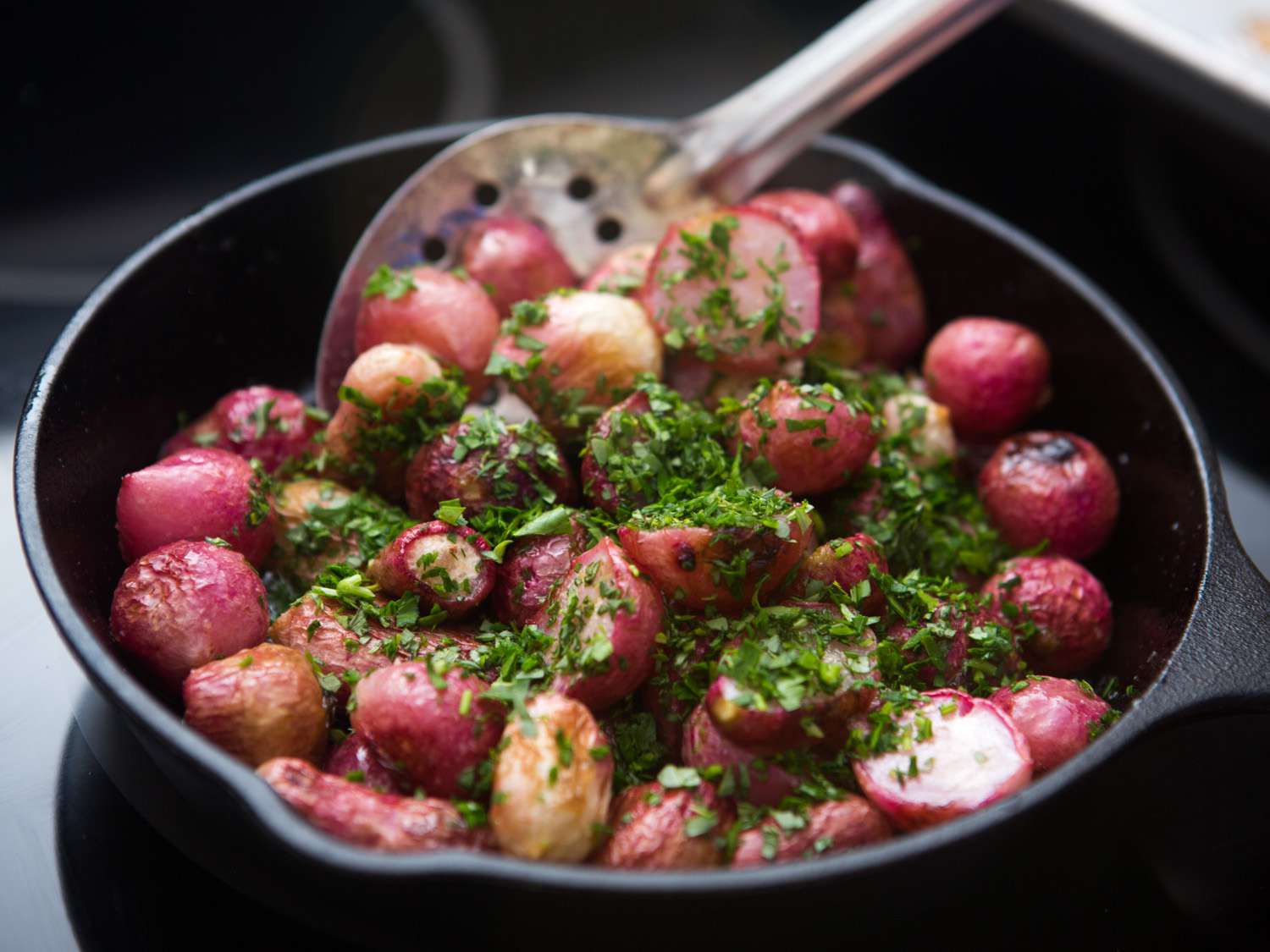 Roasted radishes in a skillet, sprinkled with minced herbs and ready to be tossed.