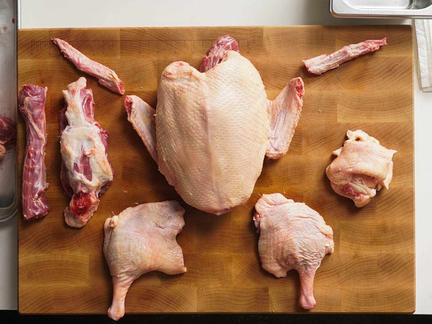 Overhead of a whole duck broken down ion a wood cutting board with two leg quarters, two wing tips, cage with breasts attached, fat and skin, backbone, and neck.