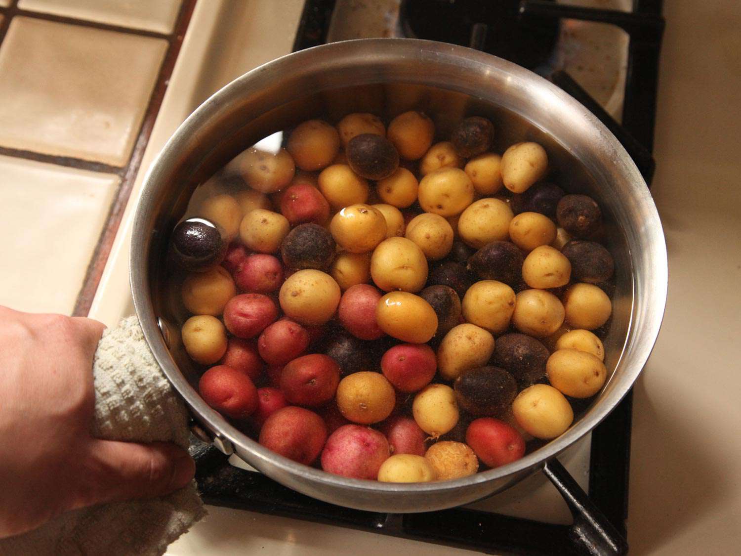 Multi-colored small new potatoes submerged in pot of water