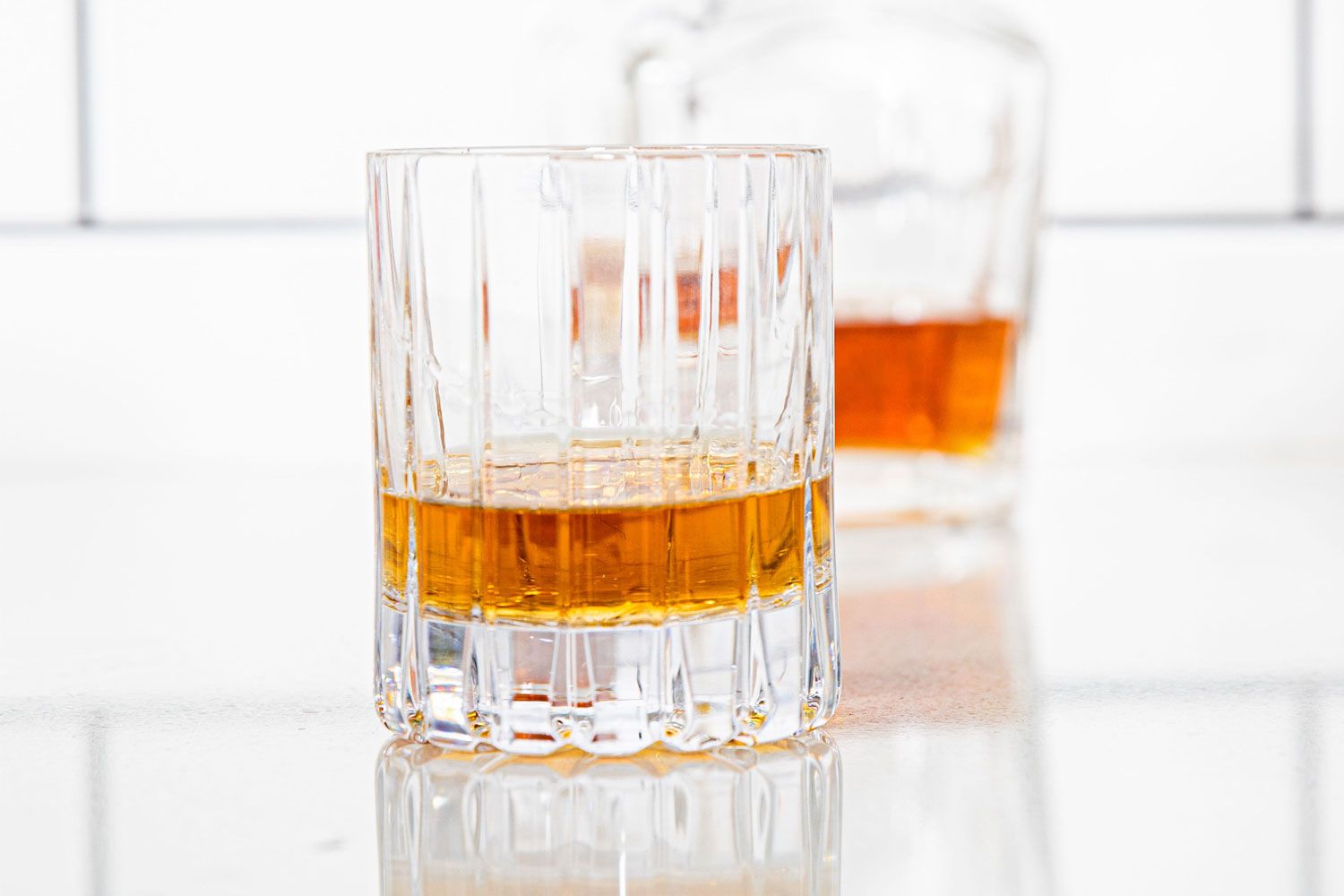 a whiskey glass with whiskey in it with a bottle of whiskey behind it