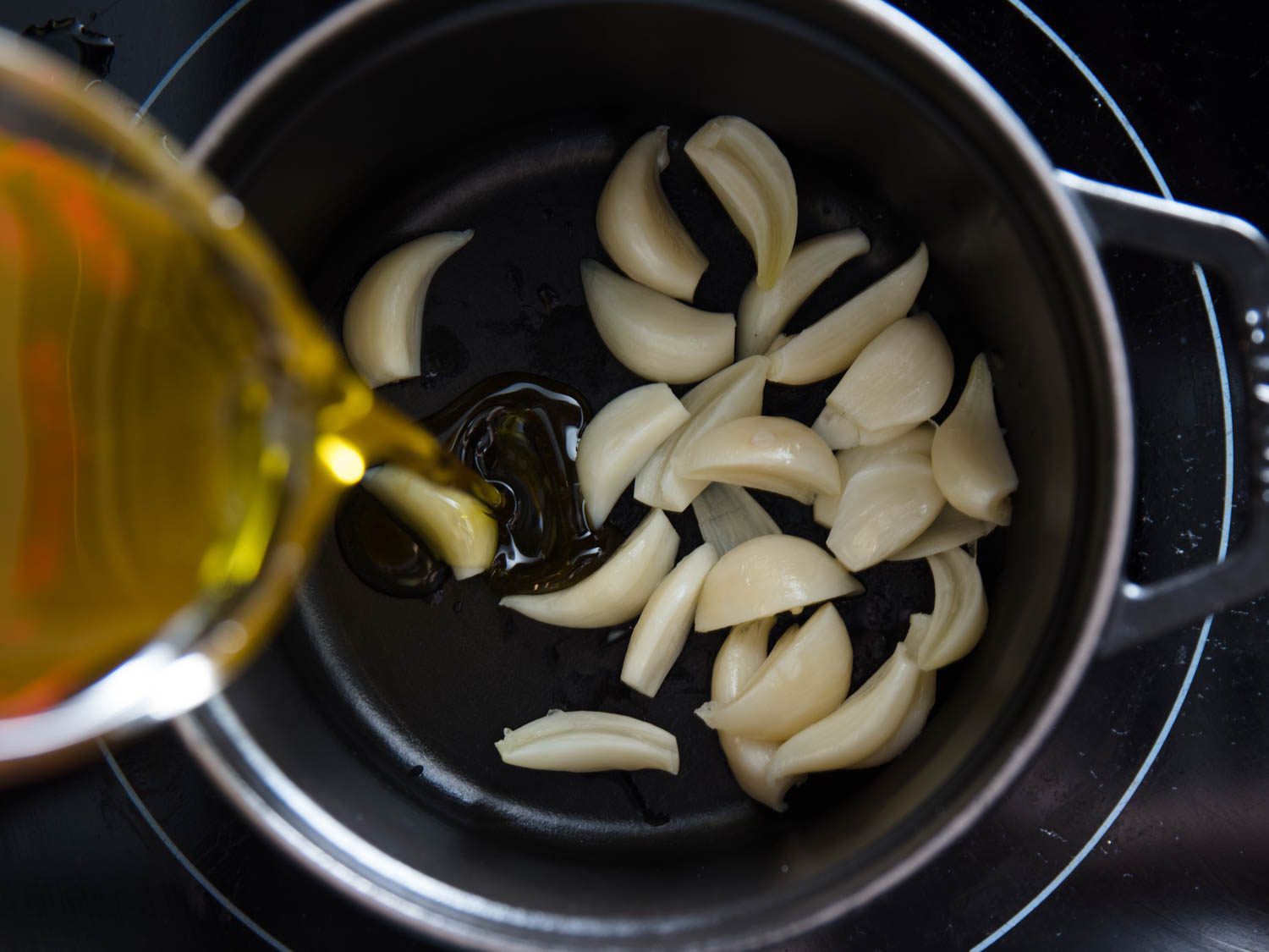 Pouring oil into pan with garlic cloves that have had their germs removed.