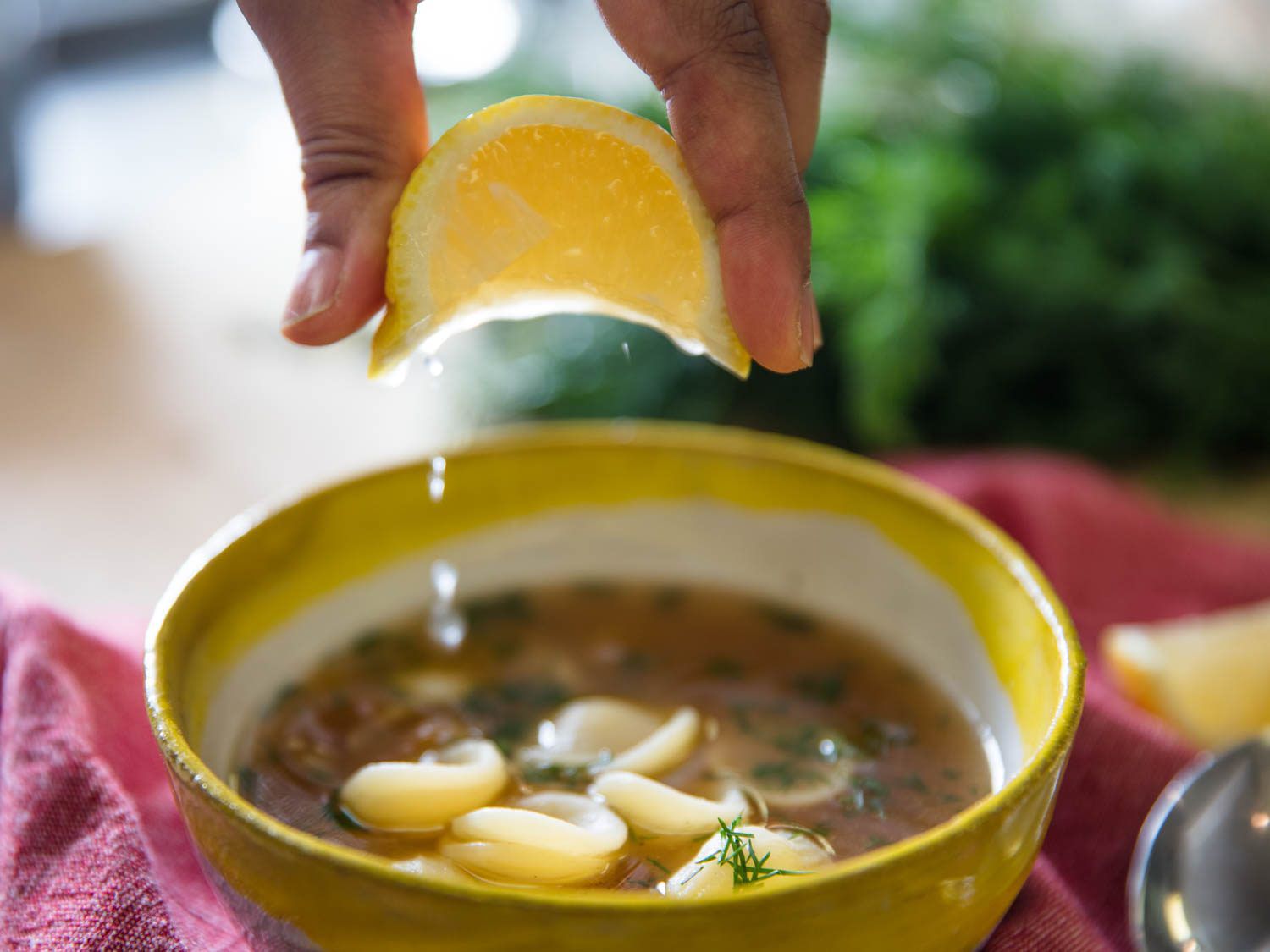 Squeezing fresh lemon juice over a bowl of homemade chicken noodle soup.