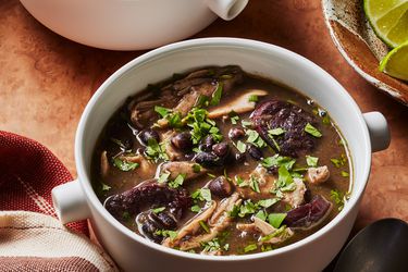 2 mugs of chicken and black bean soup with a bowl of limes on the side. 