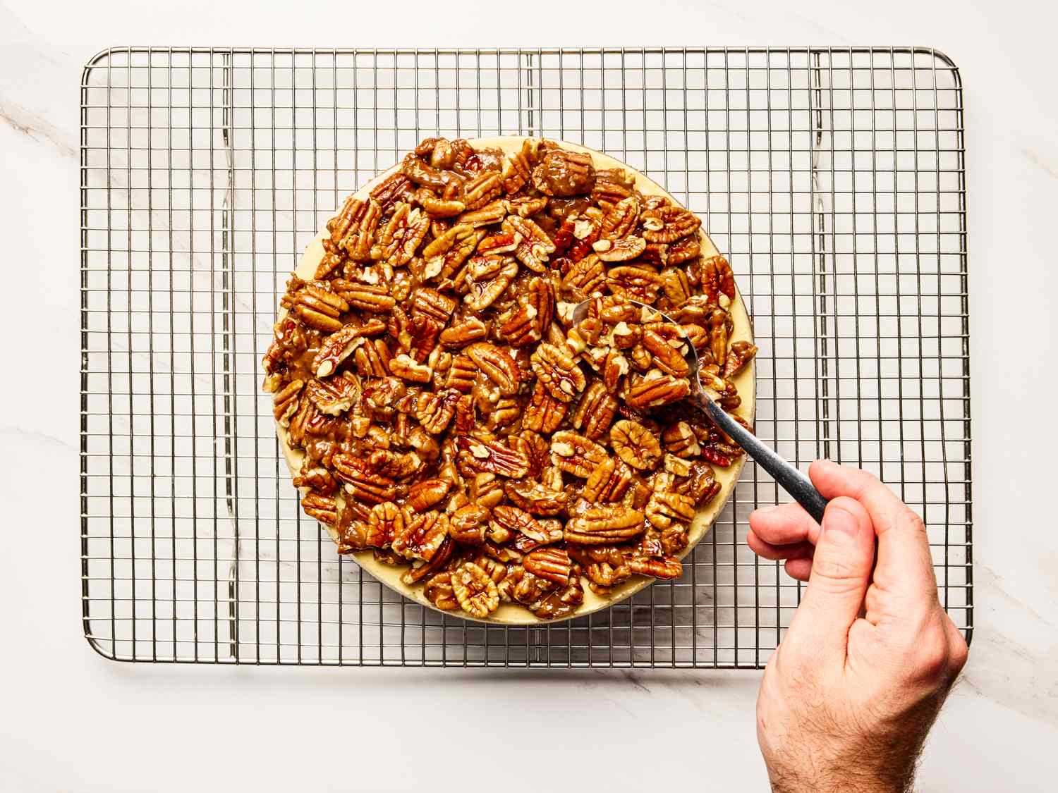 Pecan pie cheesecake placed on a cooling rack a hand using a knife on the edge of the cheesecake