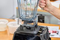 A hand lifting the Vitamix E310 Explorian Blender jar from the base