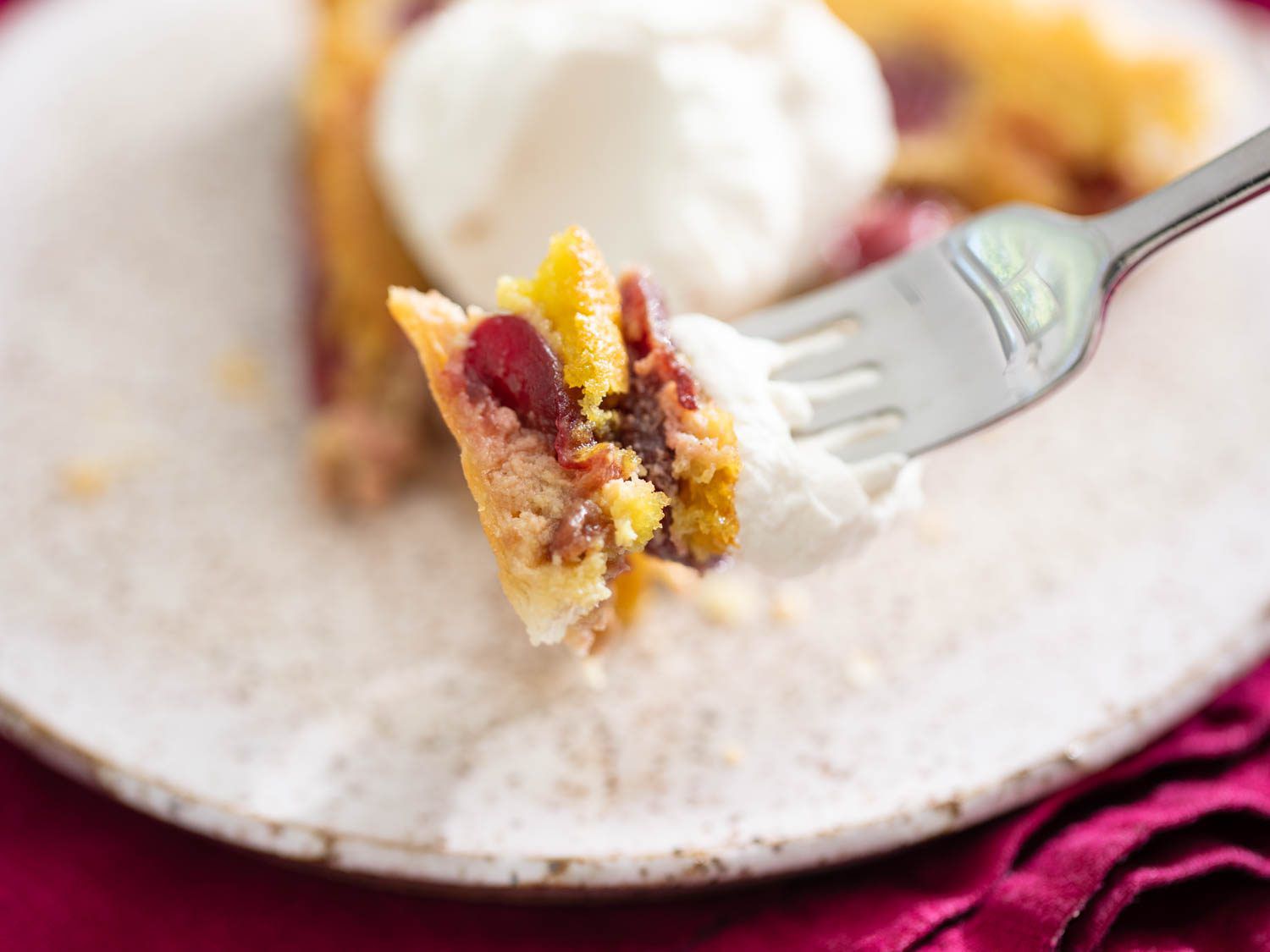 a bite of tart on a fork showing layers of flaky pastry, pistachio frangipane, baked cherries and cherry pit whipped cream