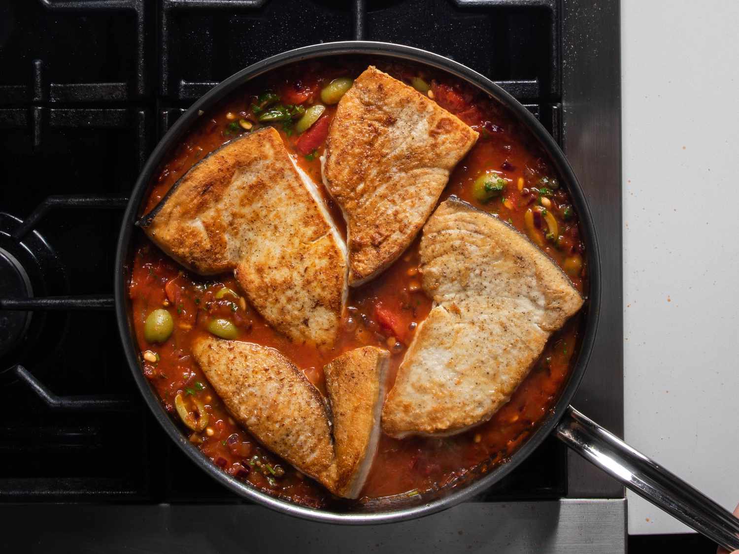 Browned swordfish steaks sit in the skillet, nestled into the sauce.