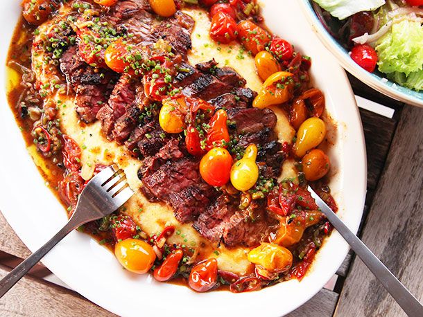 Sliced skirt steak on a bed of polenta smothered in burst cherry tomato sauce.