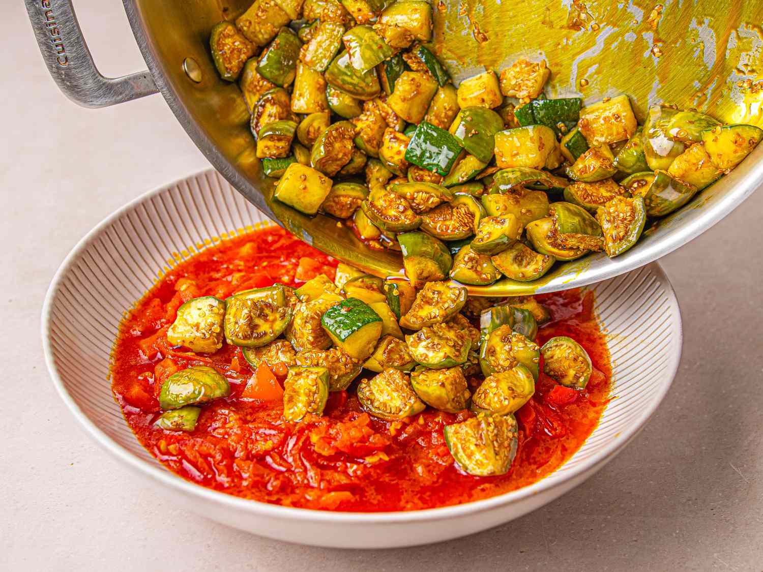 A vegetable stirfry stew being poured into a dish of tomatobased sauce