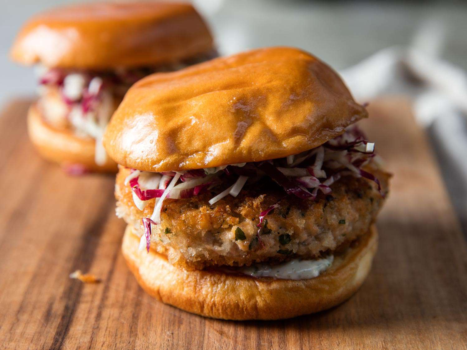 Two salmon burgers arranged on a cutting board.
