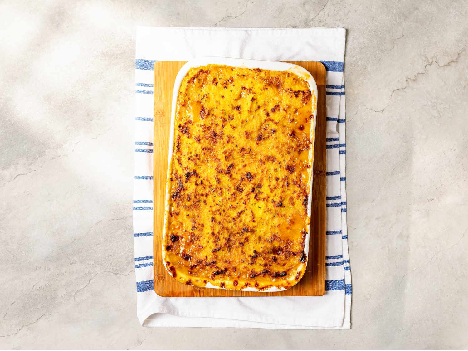 Overhead view of casserole after being baked on wooden board and towel, on top of a marble surface