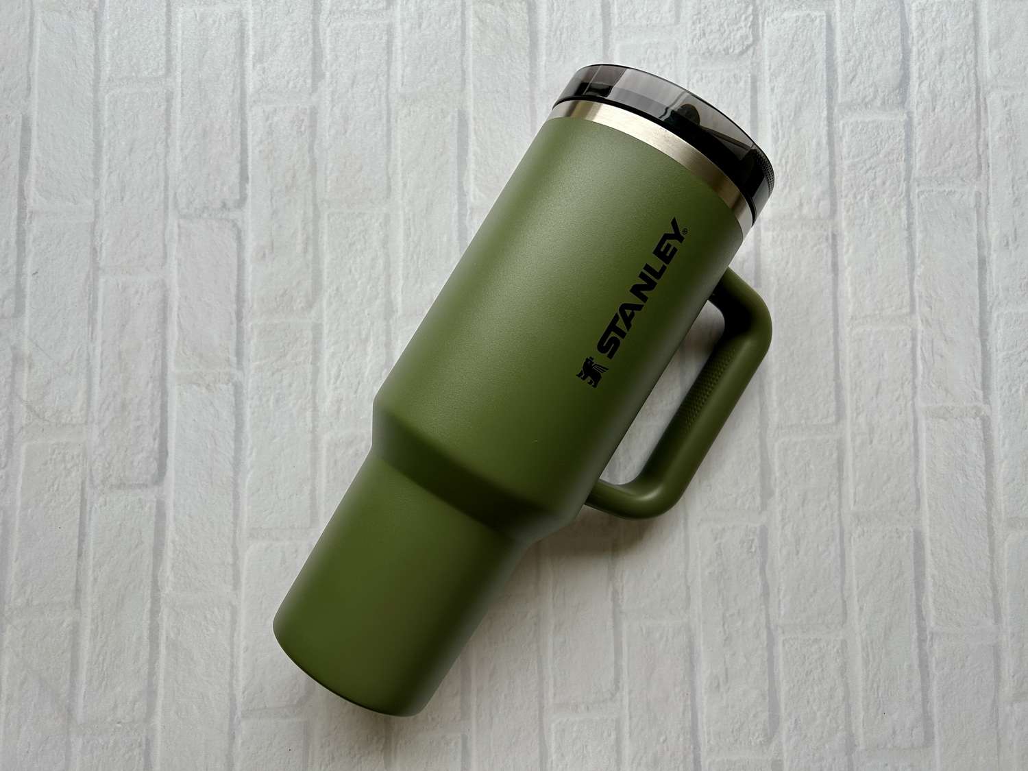 A green Stanley Quencher ProTour tumbler in front of a white brick background