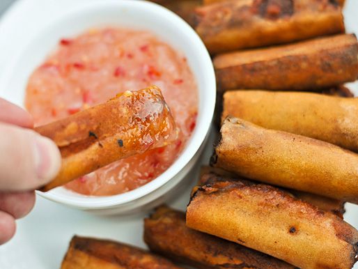 An egg roll is dipped into Thai sweet chili sauce. 