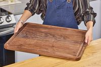A person holding a Virginia Boys Kitchens Walnut Wood Cutting Board in a kitchen setting