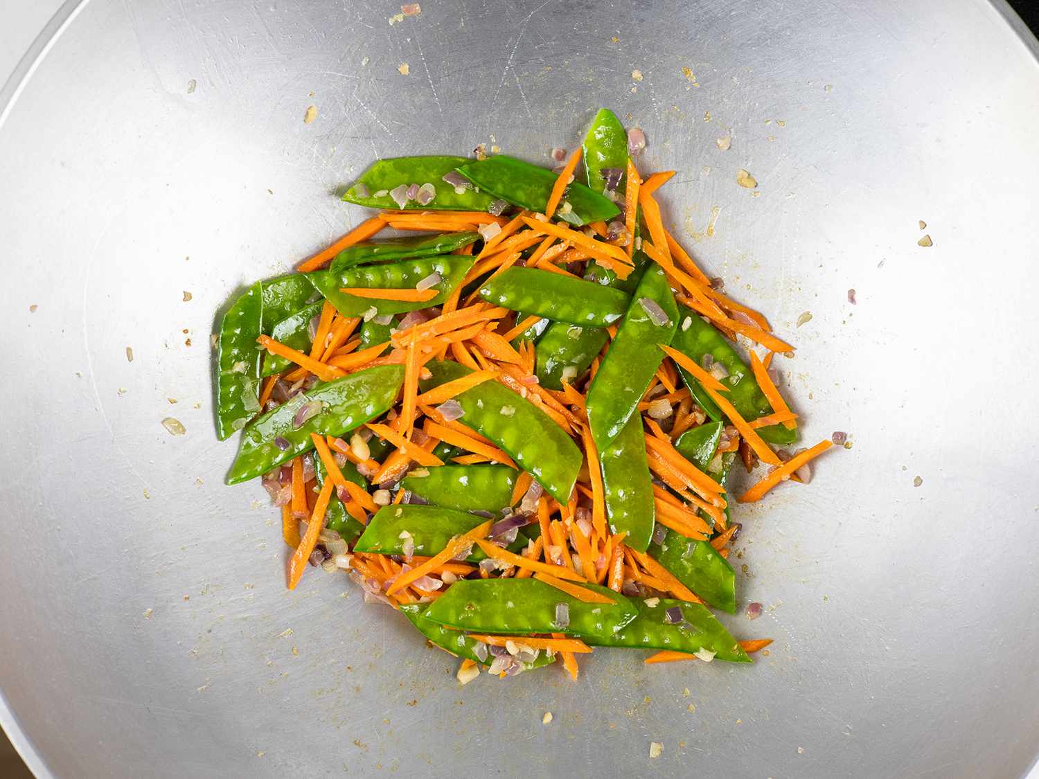 Snow peas and carrots are added to the pan.
