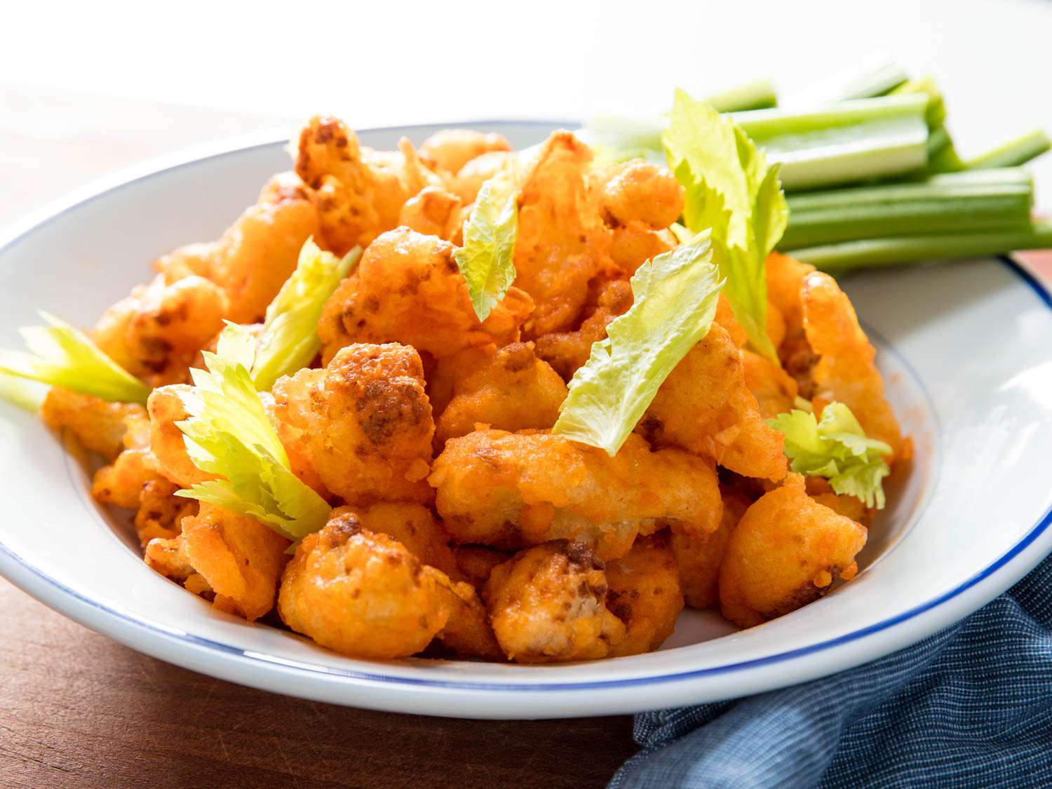 A plate of crispy buffalo fried cauliflower, with celery sticks on the side of the plate.