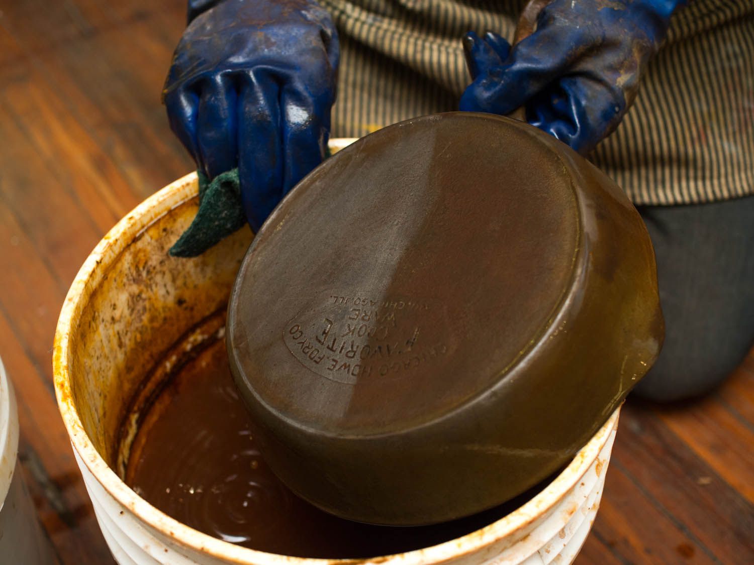 Gloved hands scrubbing the backside of a cast iron skillet to remove rust.