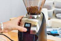 A person presses a button on the Baratza Virtuoso+ Conical Burr Coffee Grinder