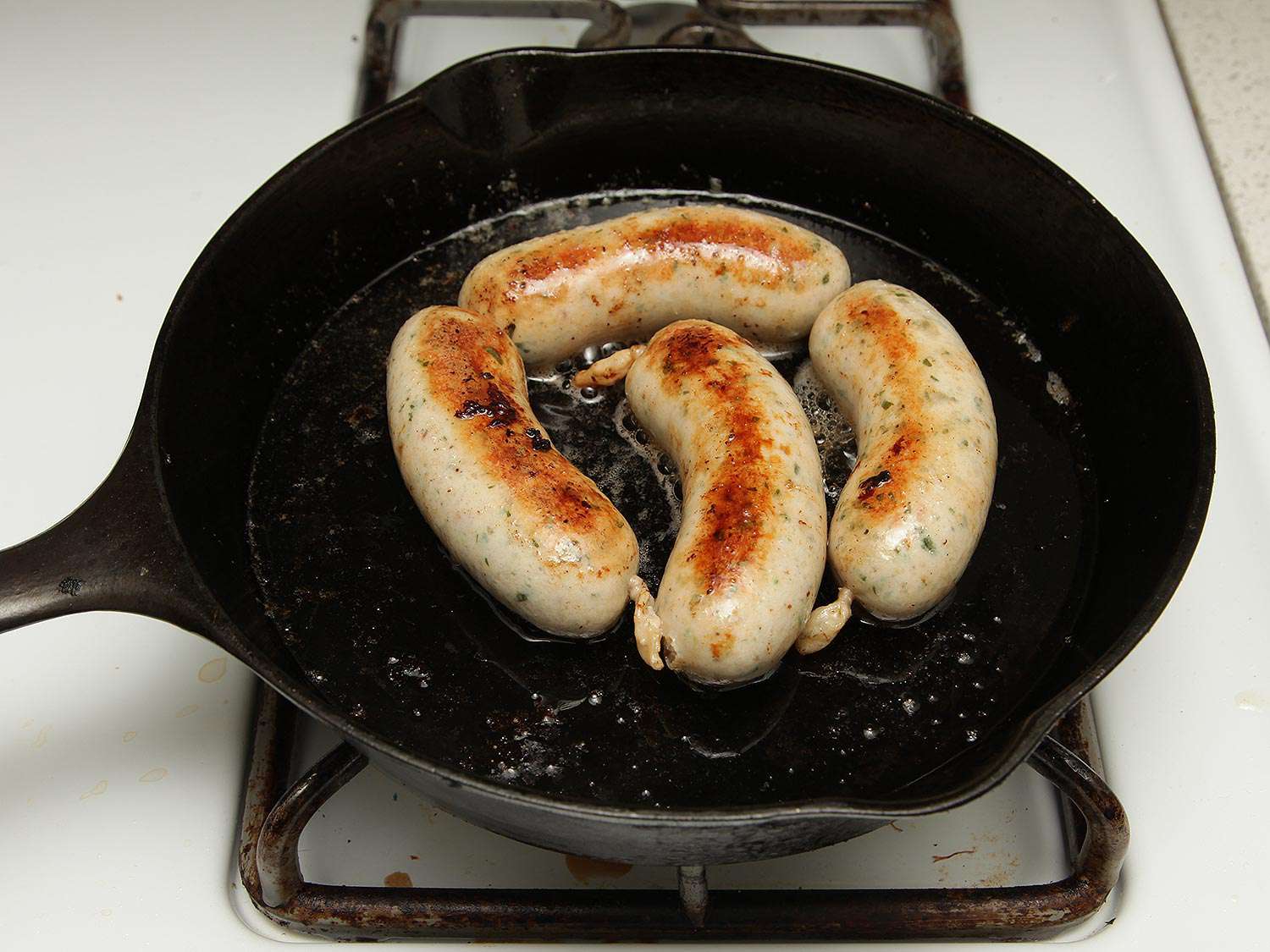 Weisswurst links browning in a cast iron skillet.