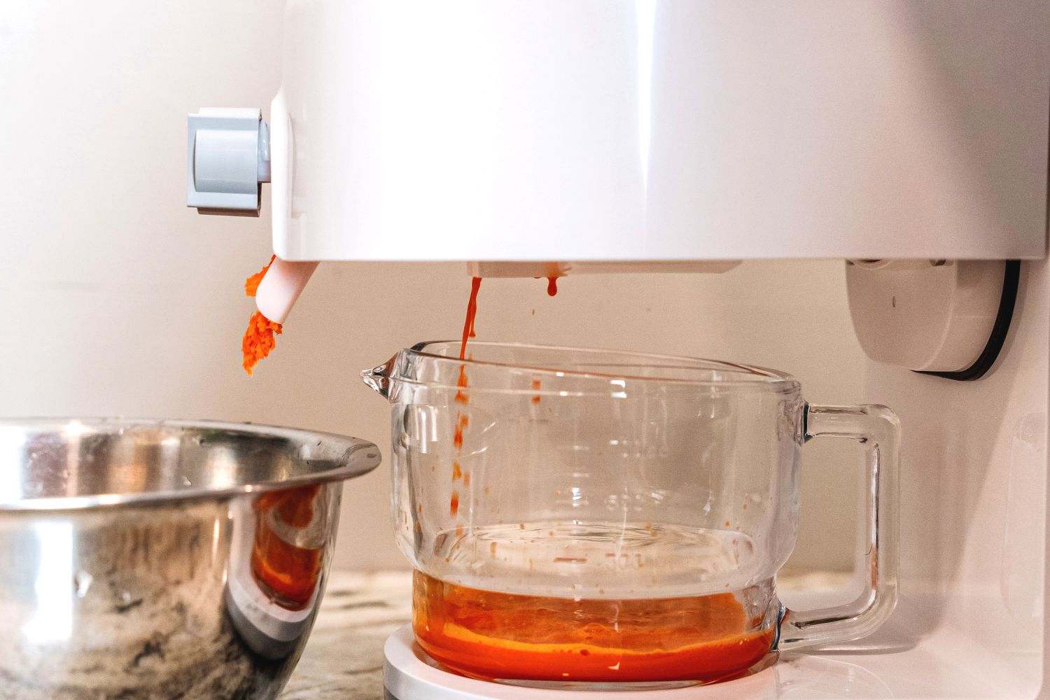 Carrot juice and pulp comes out of the Tribest Greenstar juicer and into a glass jar.