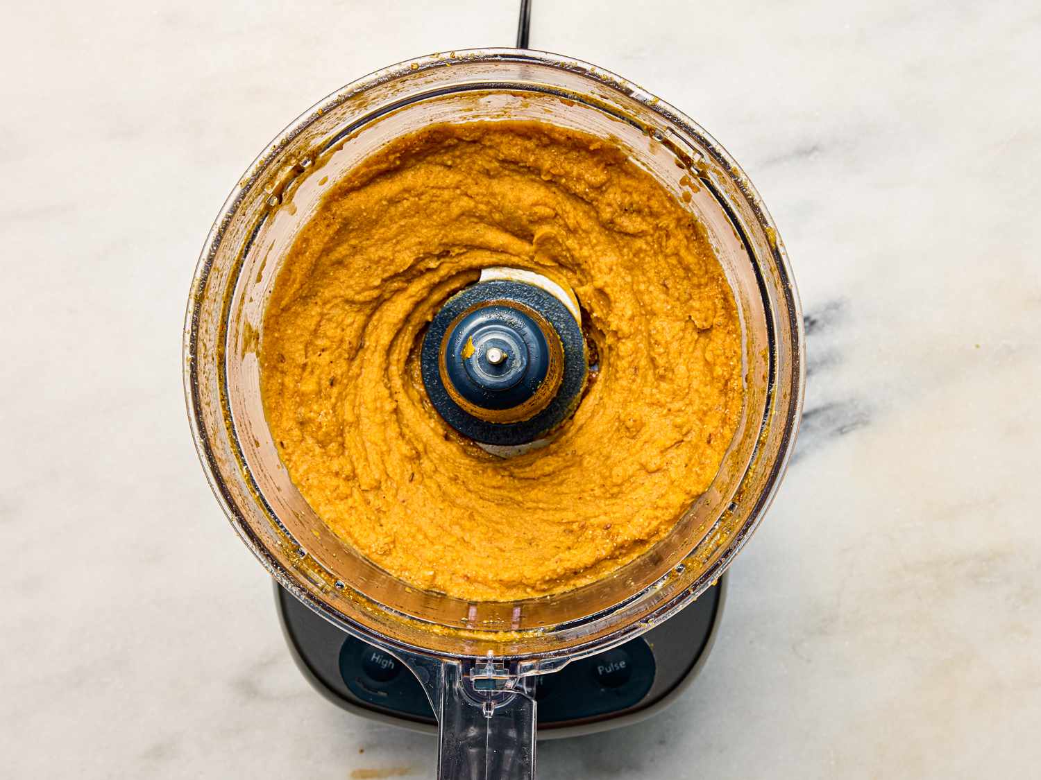 A food processor containing blended sweet potato pepita dip on a countertop