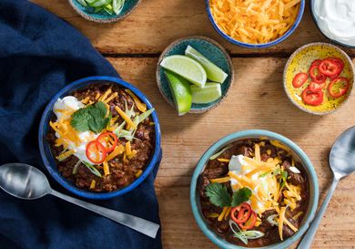 Two bowls of pressure cooker chili topped with cheese, sour cream, cilantro, chile slices, and lime wedges.