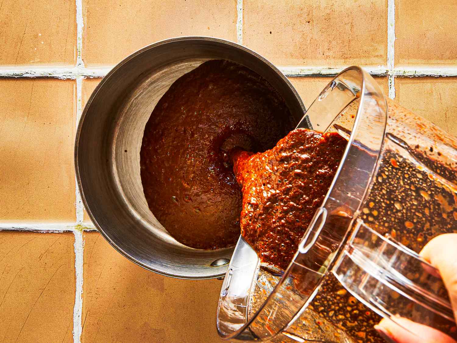 Blended sauce being poured into a saucepan on a tiled surface