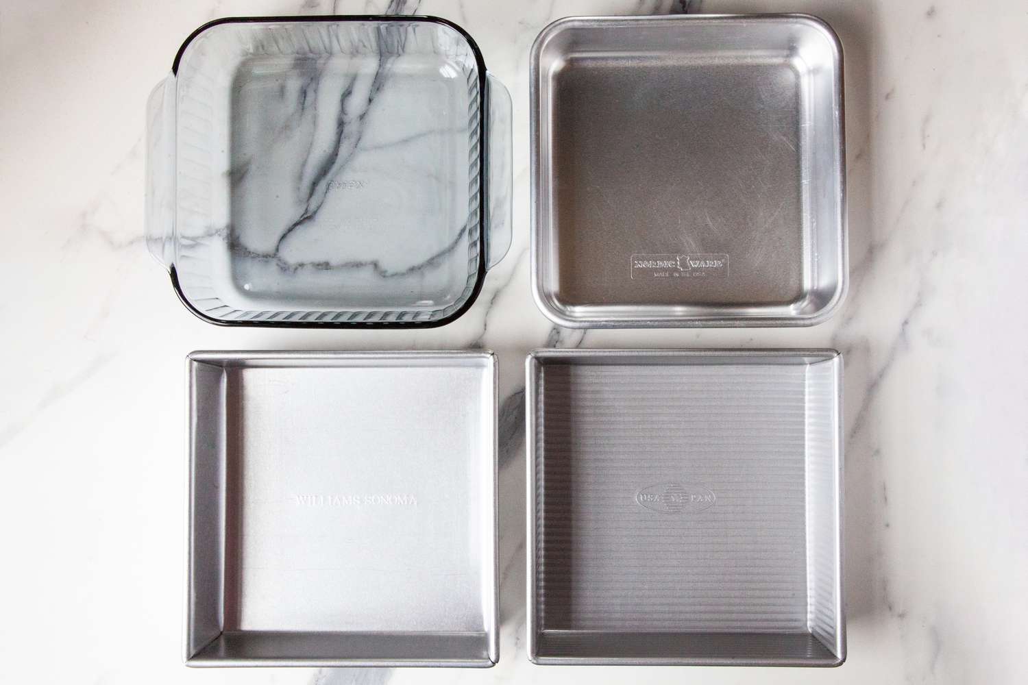 Four baking pans on a marble countertop.