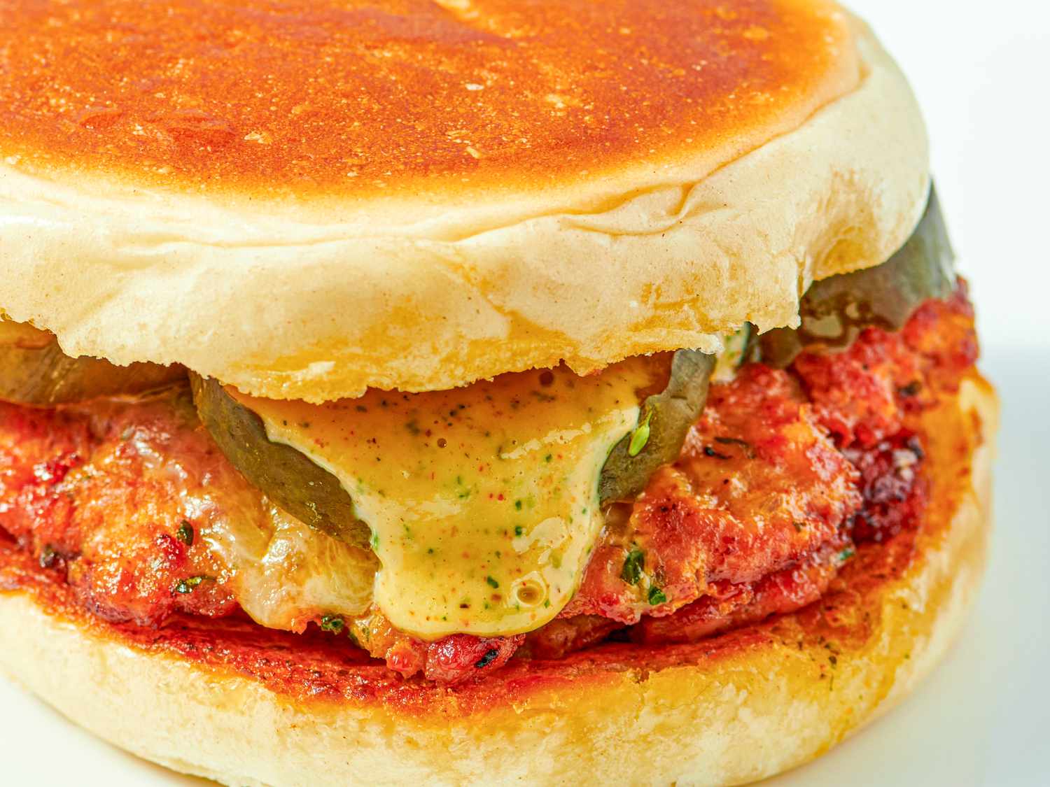 A chorizo burger with pickles and sauce in a bun