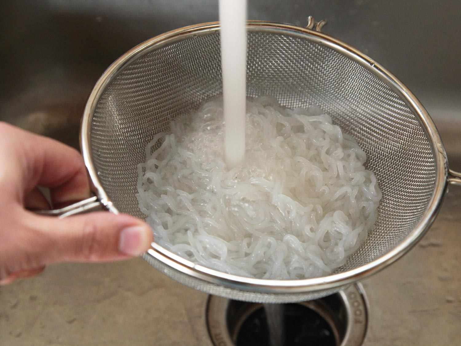 Rinsing shirataki noodles in a strainer under cold water.