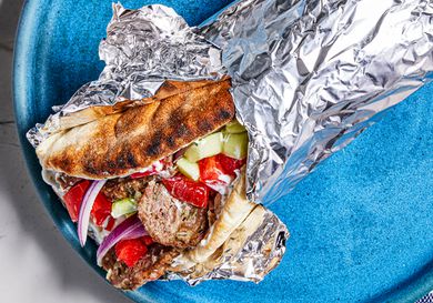 Greek-American Gryo wrapped in aluminum foil on a bright blue plate.