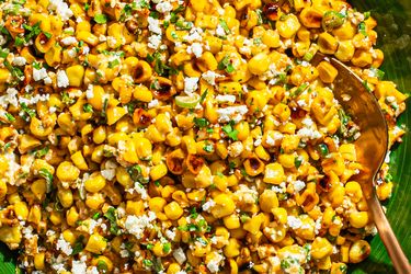 Esquites Mexican street corn salad with cheese and garnish, served in a green dish with a spoon