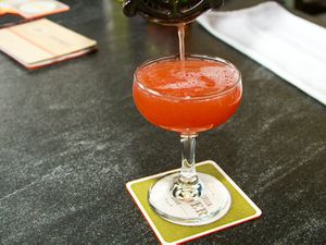A Jack Rose cocktail is strained into a coupe glass on a bartop.