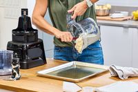 A person pours dough made in the Vitamix 12-Cup Food Processor Attachment into a greased pan