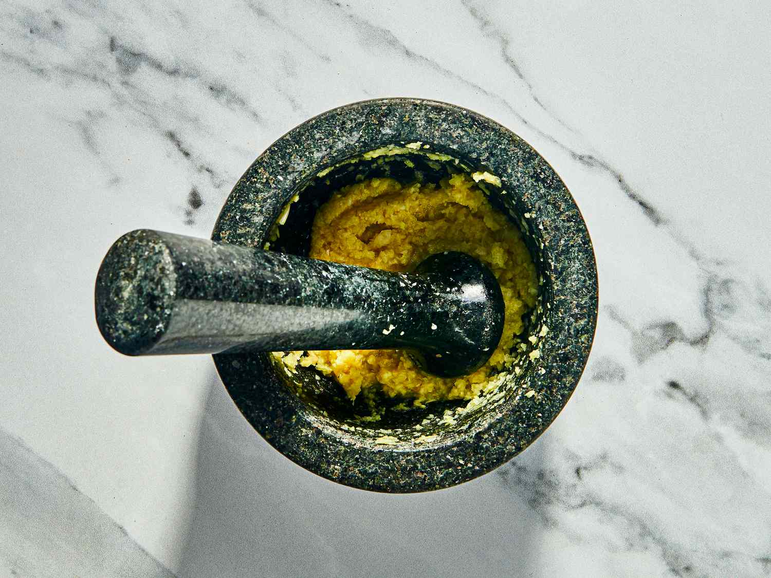 Ginger and garlic in a mortar and pestle on a white marble surface 