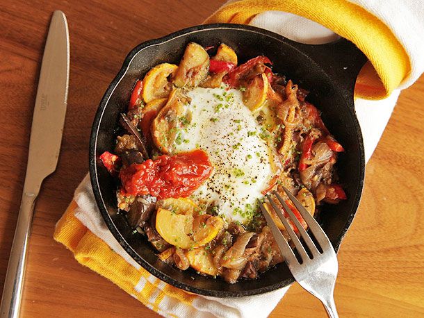 An overhead view of a skillet with eggplant, squash, and cherry tomato hash with baked eggs.