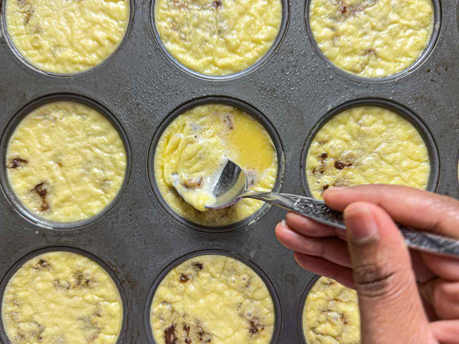 A hand scooping out a muffin-shaped egg bite with a fork from a tin, showcasing a cooking process