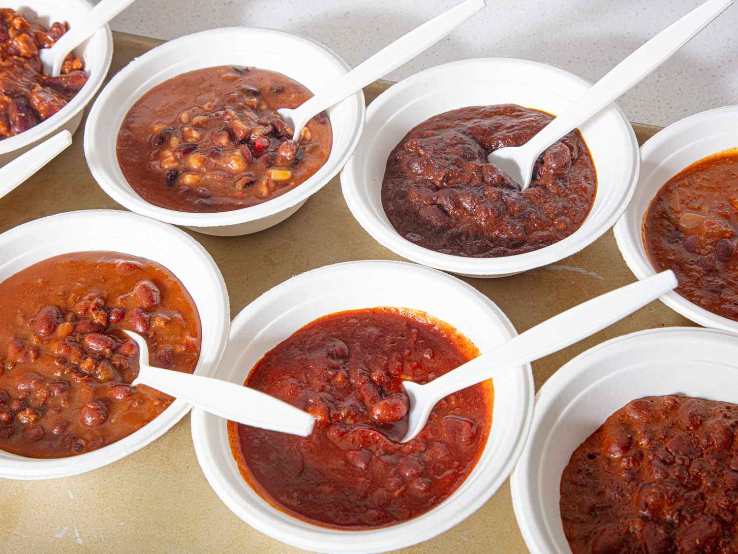 Assortment of veggie chili servings in white bowls with spoons