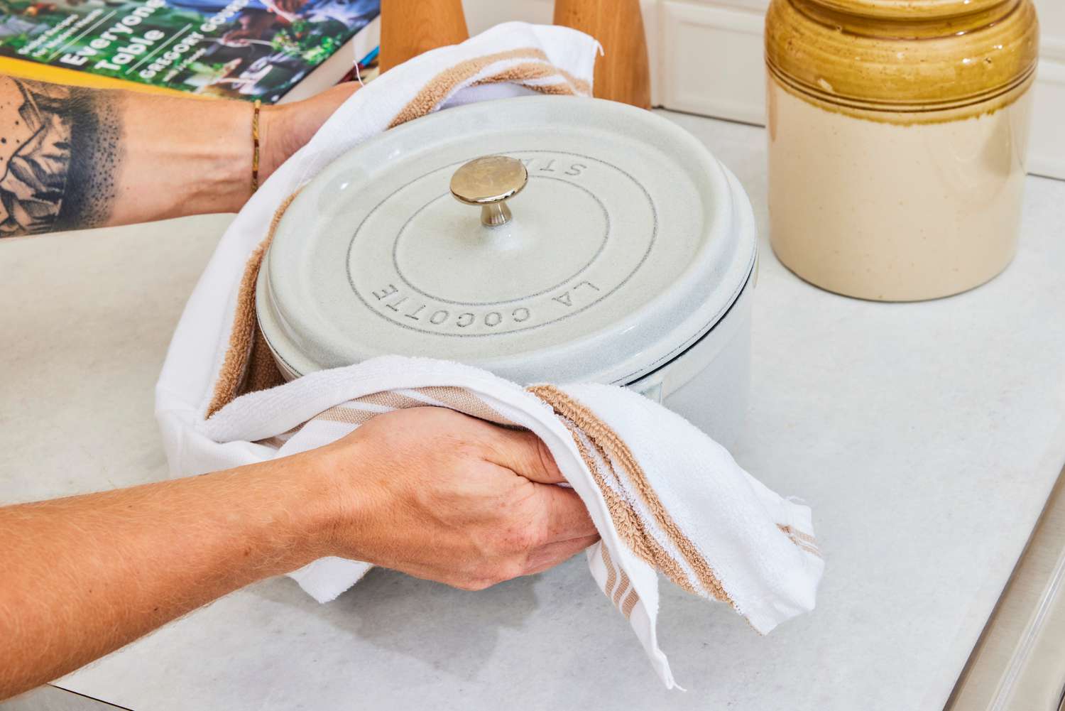 A person picking up and holding onto a Dutch oven with a kitchen towel.