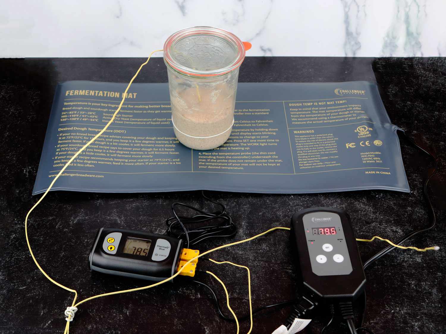 a heating mat with a sourdough starter on top and a thermocouple taking the temperature