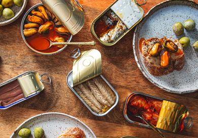 An arrangement of various open tins of fish displayed with accompaniments like olives and bread
