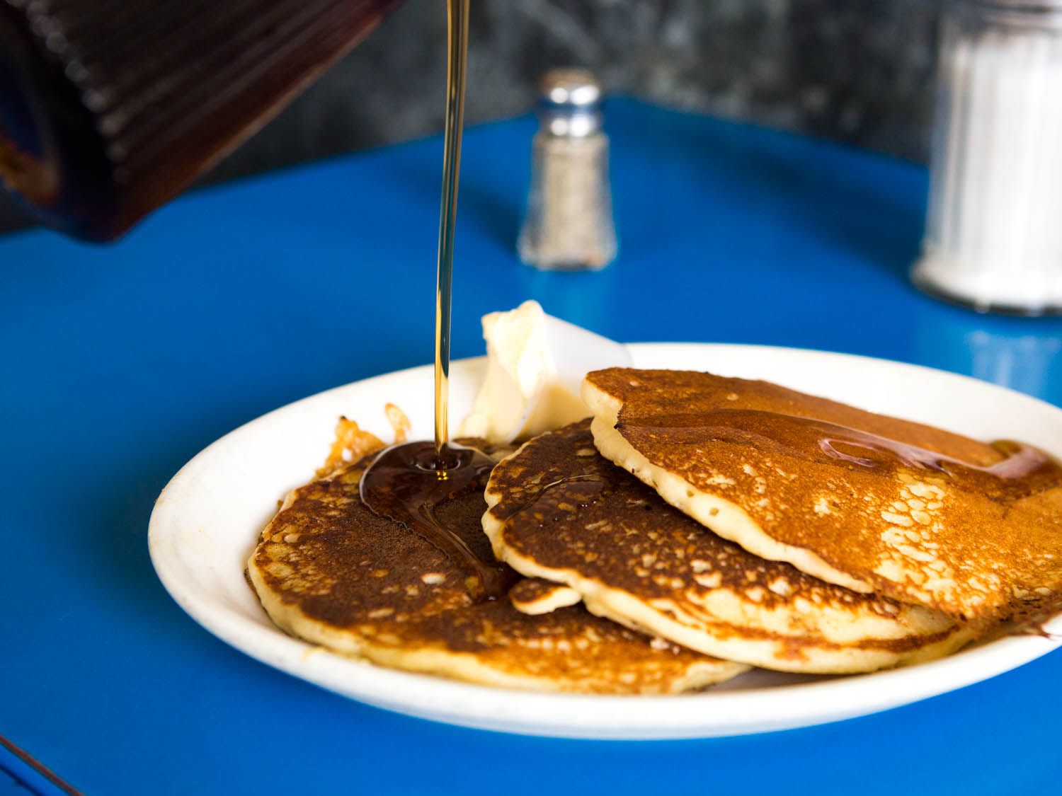 A plate with three pancakes, butter, and syrup being poured over the pancakes.