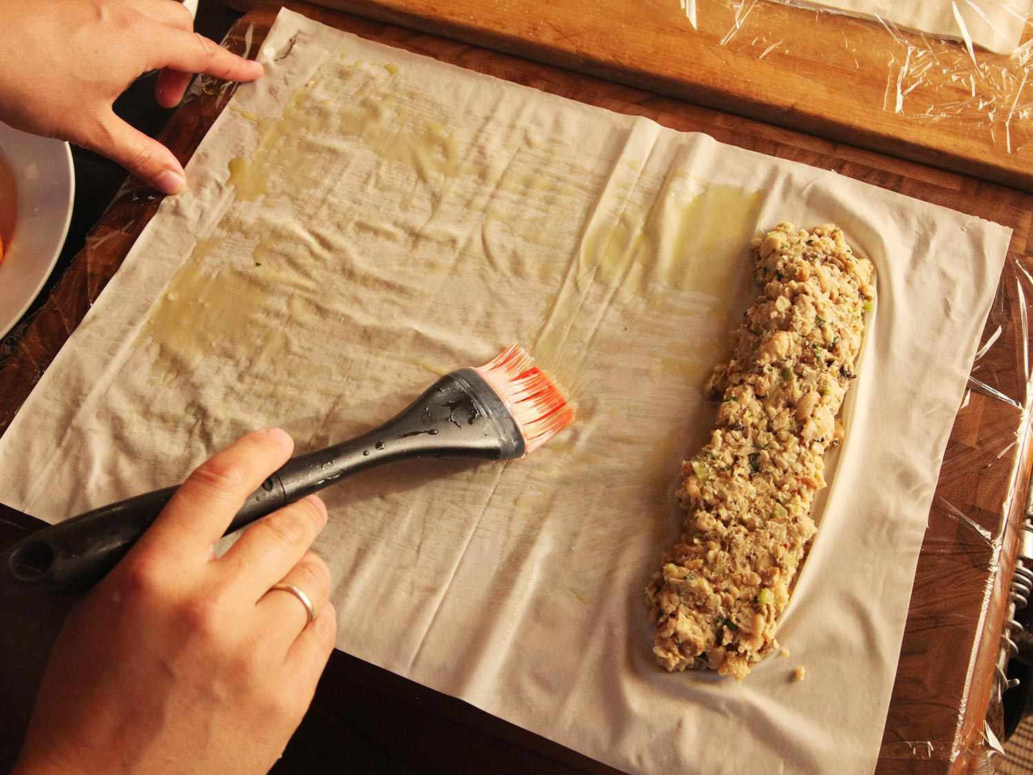 Brushing olive oil into phyllo sheet containing narrow strip of bean mixture on the right hand side.